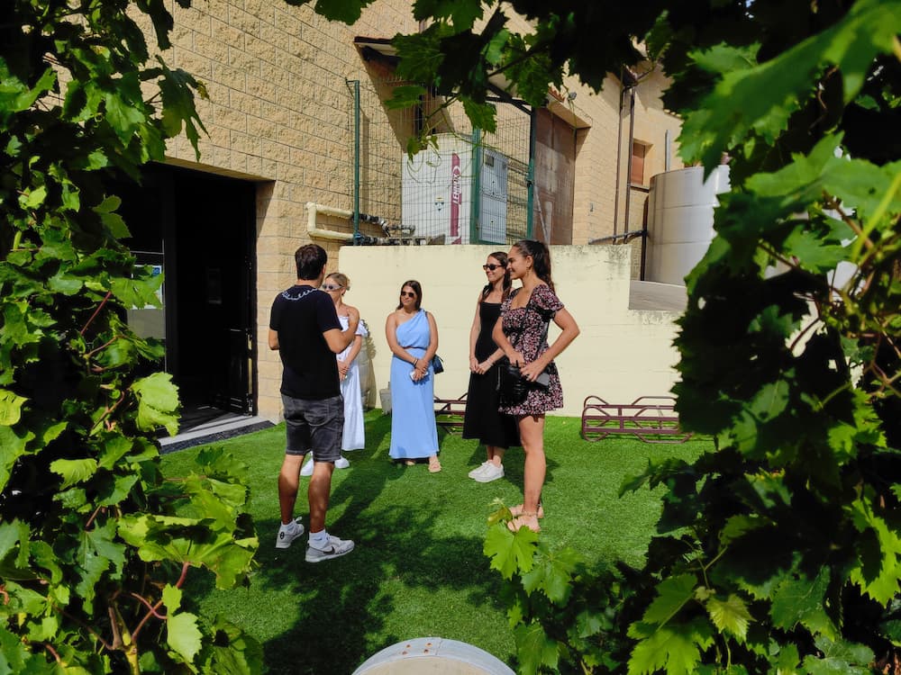 A tour guide talking to four young women from New York in a lush green garden area framed by grapevines, part of an immersive private Rioja wine tour experience with North Coast Tours.